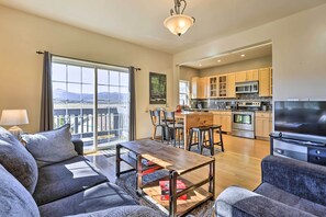 A spacious living room with a sofa, coffee table, and a TV. The kitchen is visible with modern appliances and wooden cabinets. - Lovely Fraser Retreat w/ Hot Tub & Fire Pit! (Fraser)