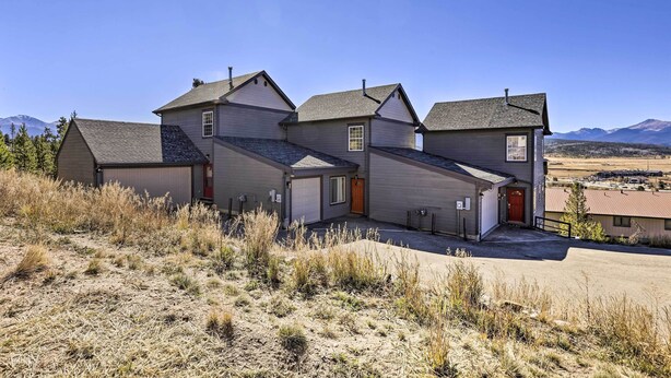A modern residential building with multiple garage doors, a red door, and a view of mountains in the background. - Lovely Fraser Retreat w/ Hot Tub & Fire Pit! (Fraser)