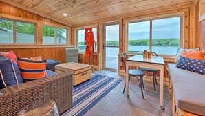 L’intérieur d’une cabane comprend un coin repas, des sièges et de grandes fenêtres donnant sur un lac.