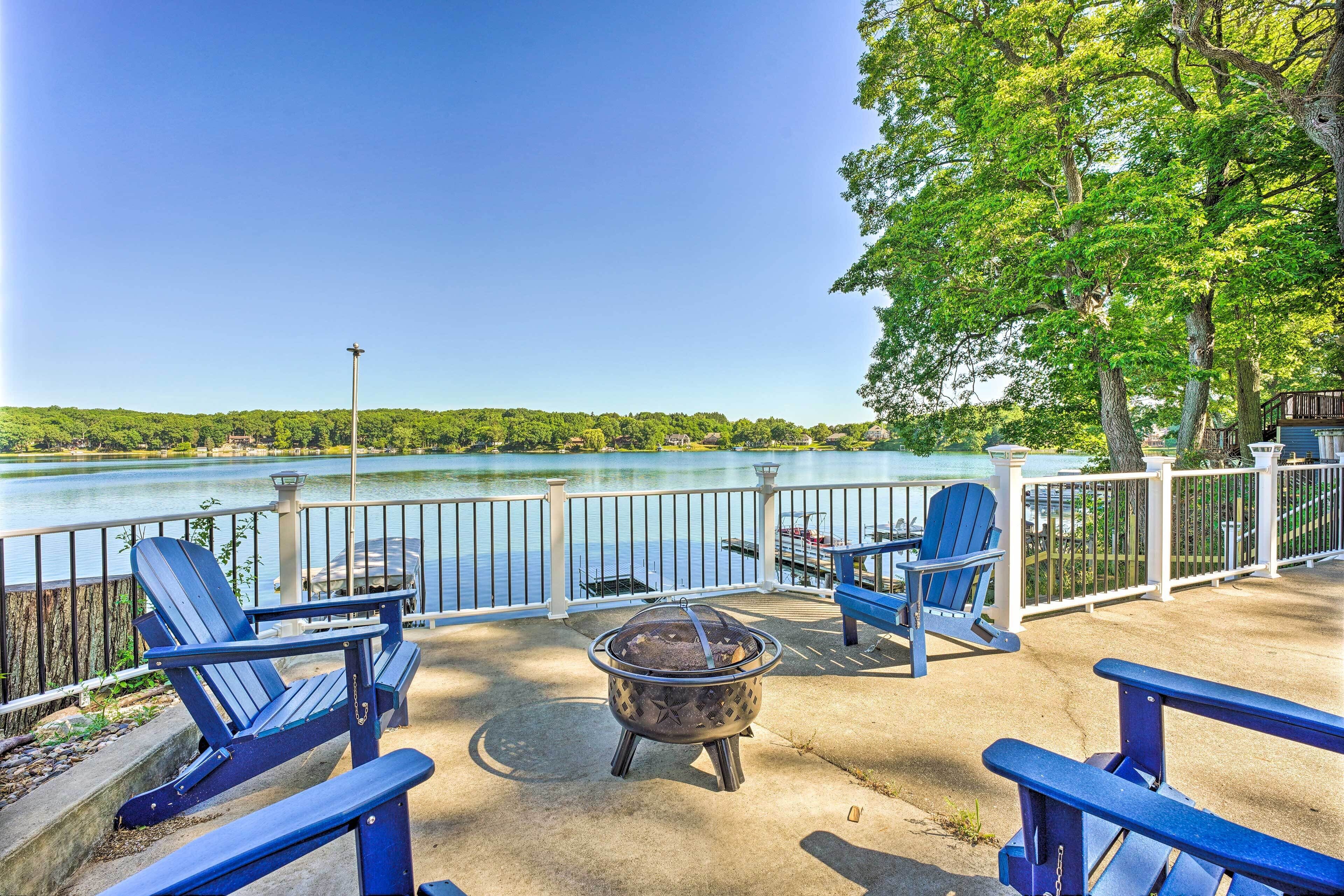 A deck with Adirondack chairs, a fire pit, and a view of a lake.