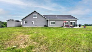 A two-story house with a large front lawn, a garage, and a patio area with outdoor furniture. - Quiet Retreat w/ Kayak & Patio, Walk to Lake! (Audubon)