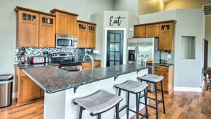 A modern kitchen with wooden cabinets, a granite countertop, and a central island with bar stools. - Quiet Retreat w/ Kayak & Patio, Walk to Lake! (Audubon)