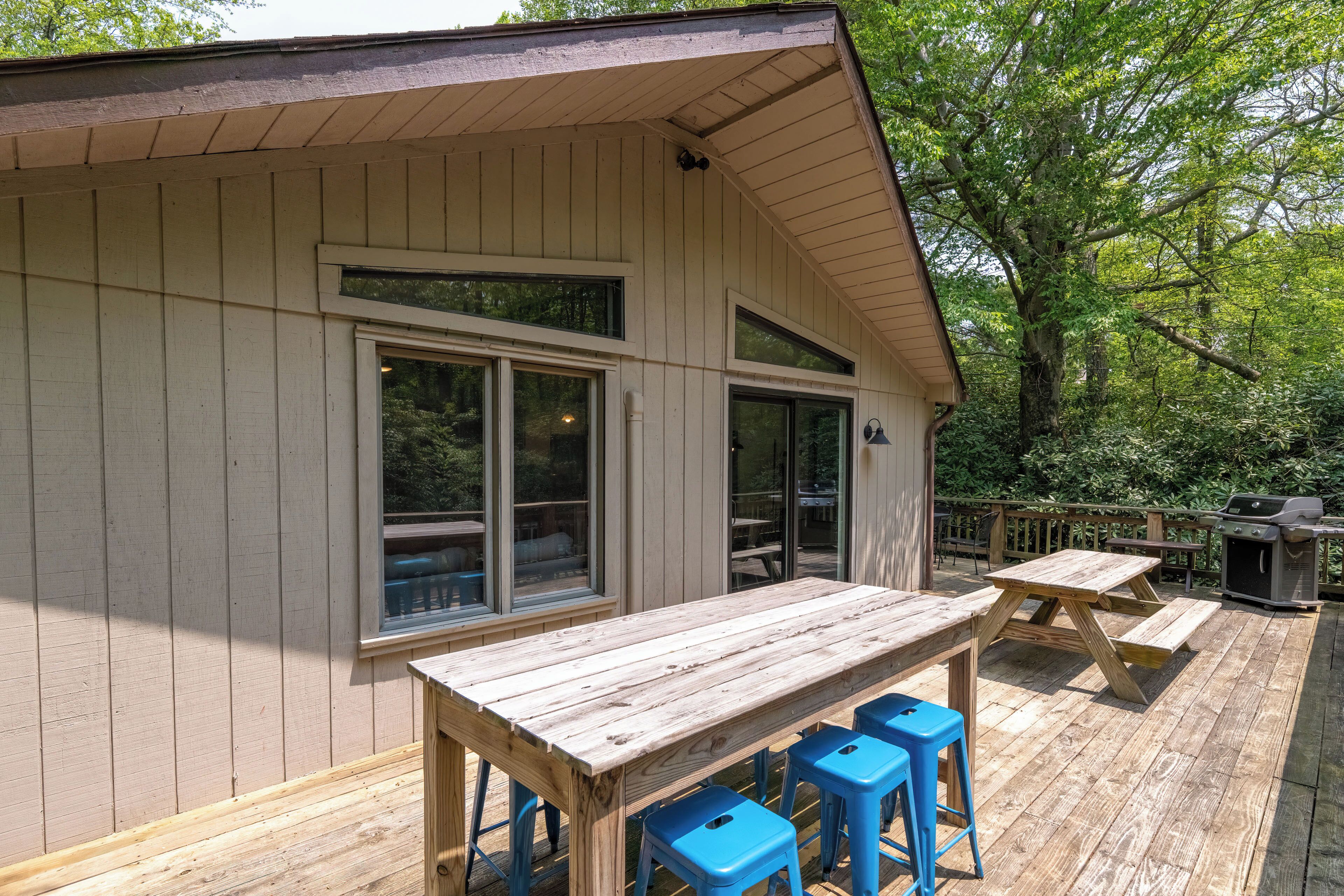 A wooden deck with a picnic table and blue stools, surrounded by a wooden building with large windows.