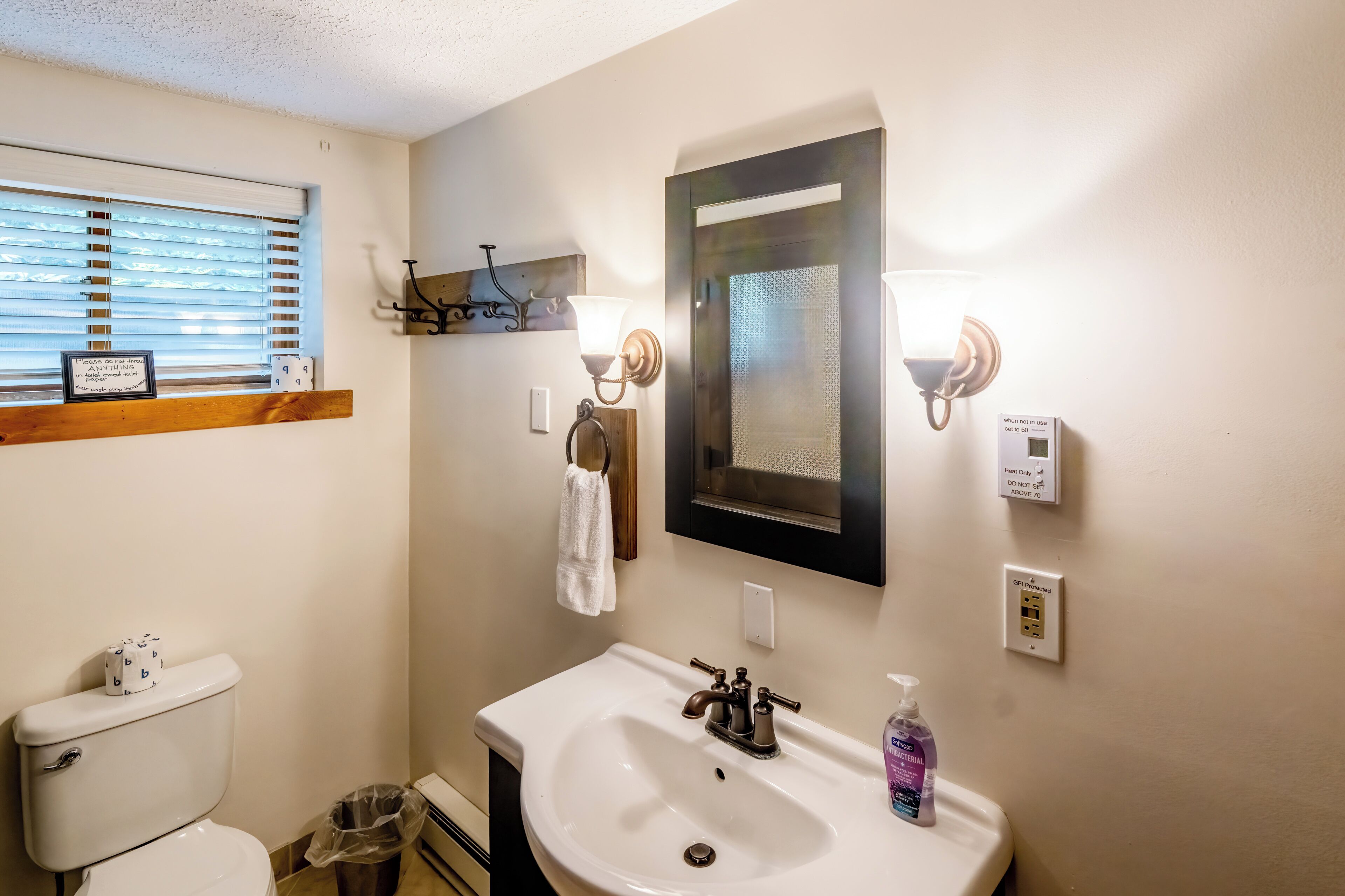 A bathroom with a toilet, sink, and window with blinds.