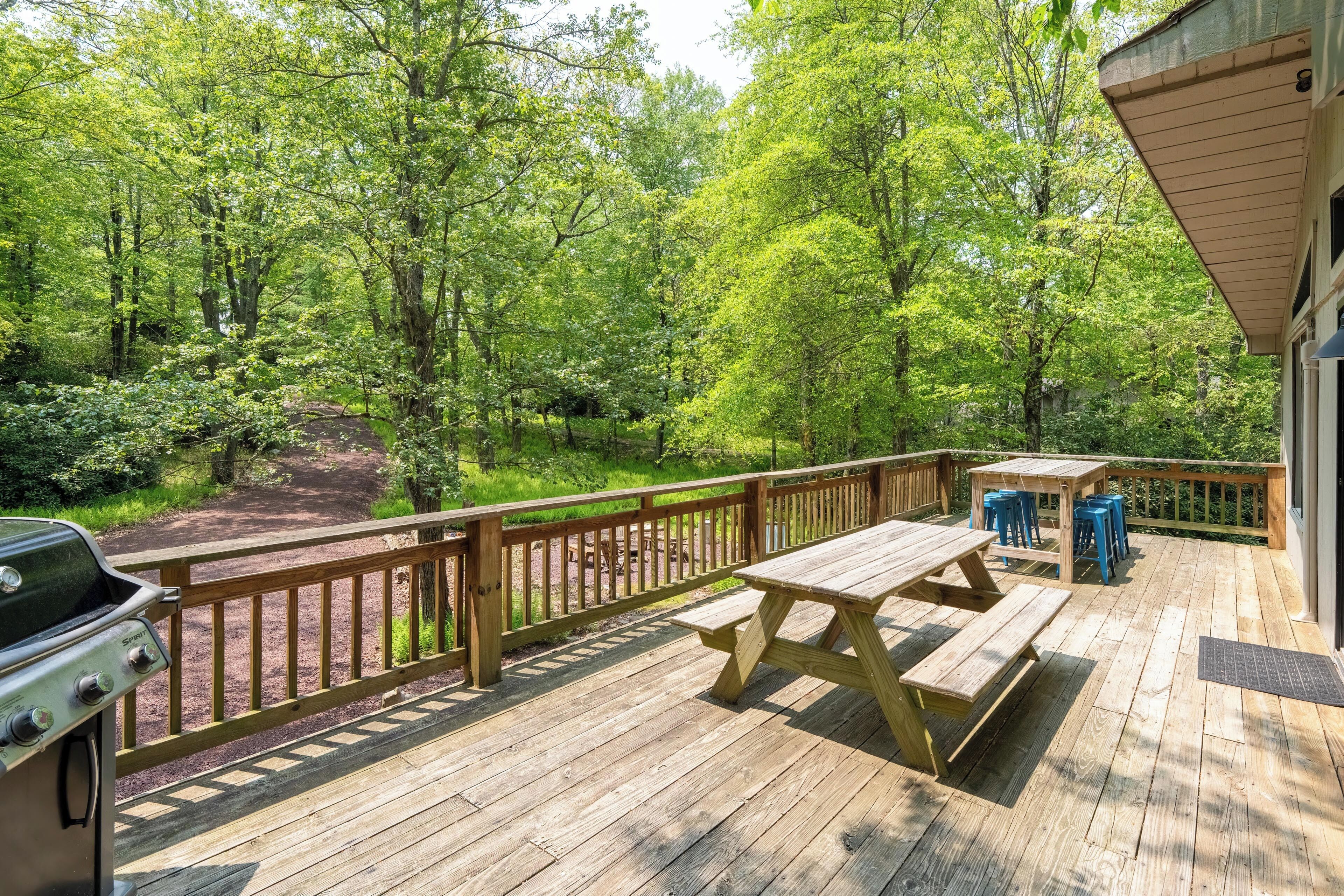 A wooden deck with picnic tables and a grill, surrounded by dense forest.