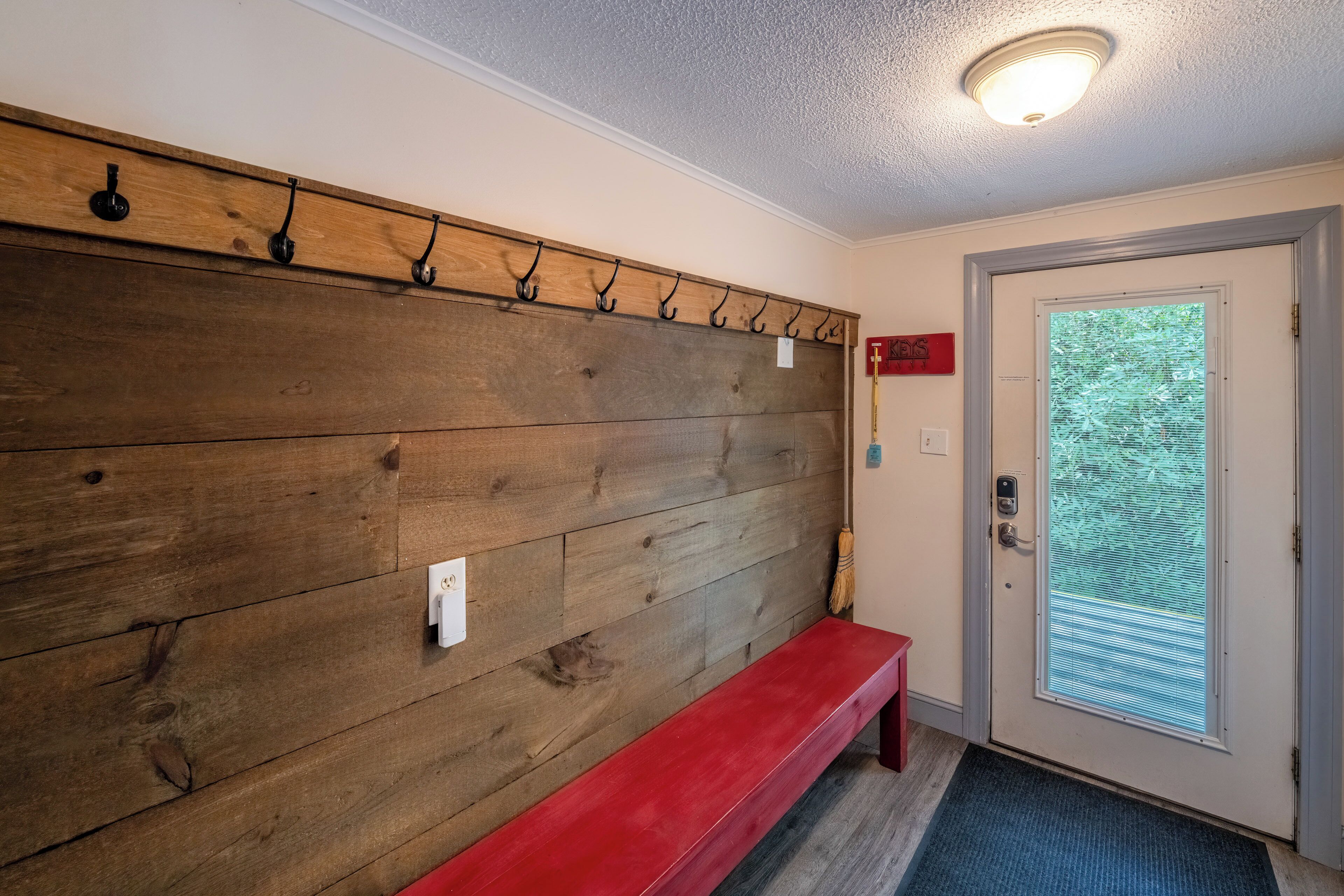 A hallway with a wooden wall, a red bench, a door with a window, and a light fixture.