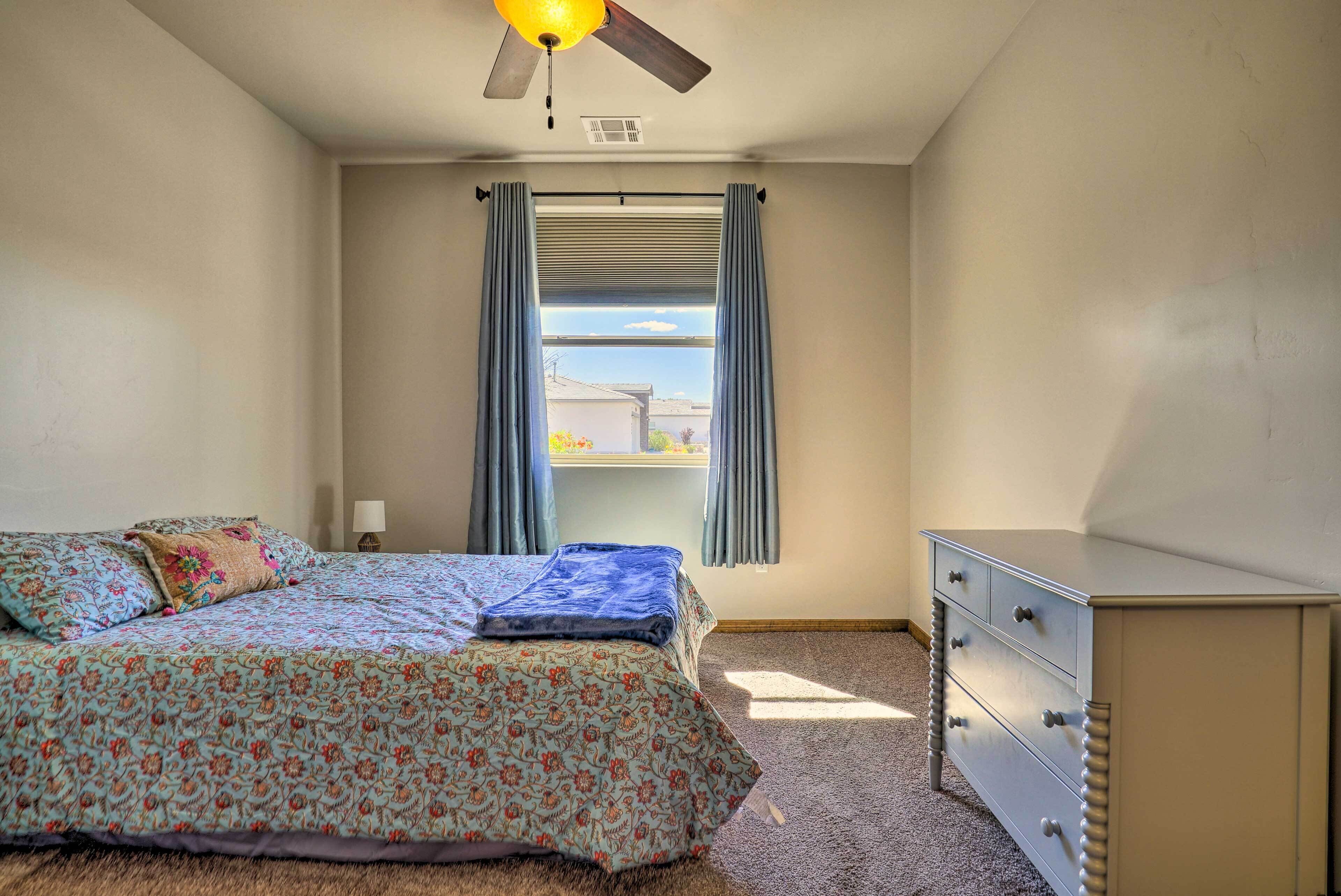 Ein Schlafzimmer mit Bett, Kommode, Deckenventilator und einem Fenster mit Vorhängen.