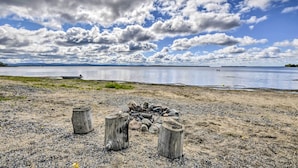 A beach with a fire pit surrounded by rocks, a wooden post, and a bench. - Cozy Lake Champlain Cottage w/ Private Beach! (North Hero)