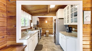 A wooden cabin kitchen with white cabinets, granite countertops, a refrigerator, and a coffee maker. - Cozy Lake Champlain Cottage w/ Private Beach! (North Hero)