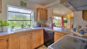 A modern kitchen with wooden cabinets, a dishwasher, a large window, and various plants.