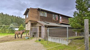 A stable with a horse, a wooden building with a balcony, and a fenced area.