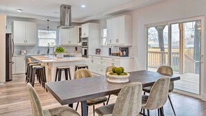 A modern kitchen with white cabinets, a central island, and a dining area with a dark table and chairs. - Indianapolis Vacation Home: 3 Mi to Dtwn! (Indianapolis)