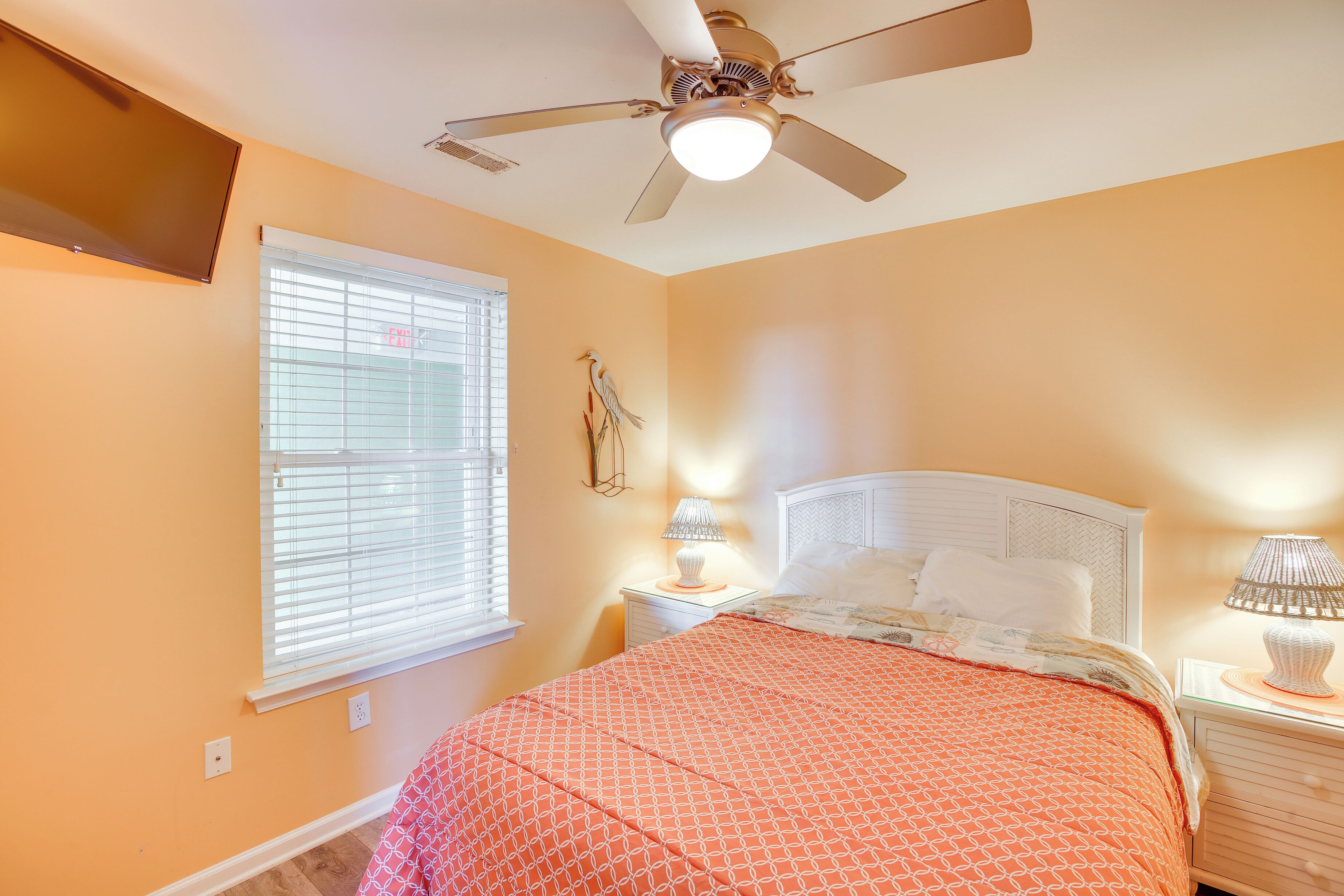 Une chambre à coucher avec un lit, un ventilateur de plafond, une table de chevet avec une lampe et une fenêtre avec des stores.
