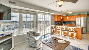 Un salón espacioso con balcón, un comedor con sillas de madera y una cocina con armarios de madera y un refrigerador de acero inoxidable.