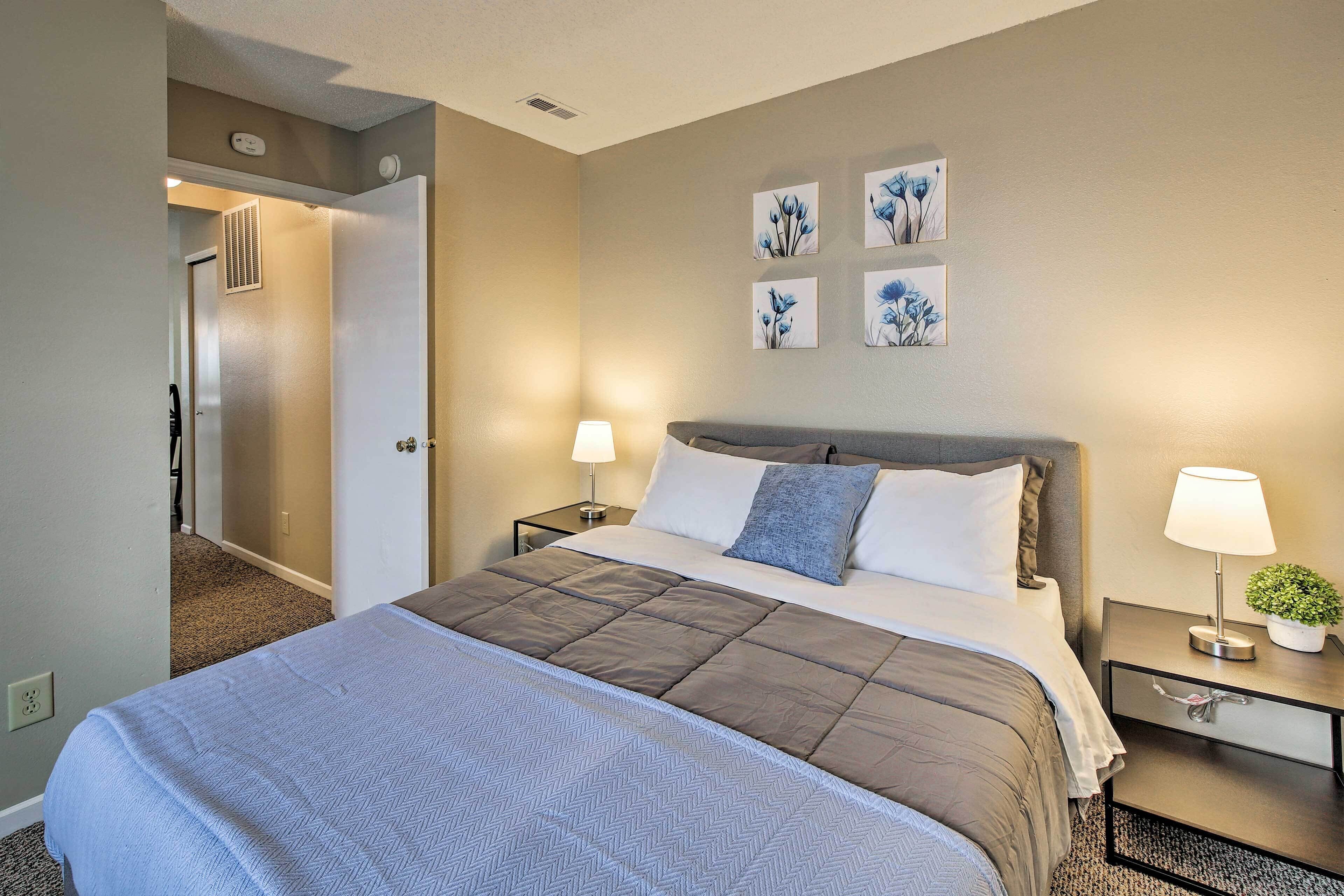 A hotel room with a large bed, two bedside tables, a wall-mounted lamp, and a door leading to a hallway.