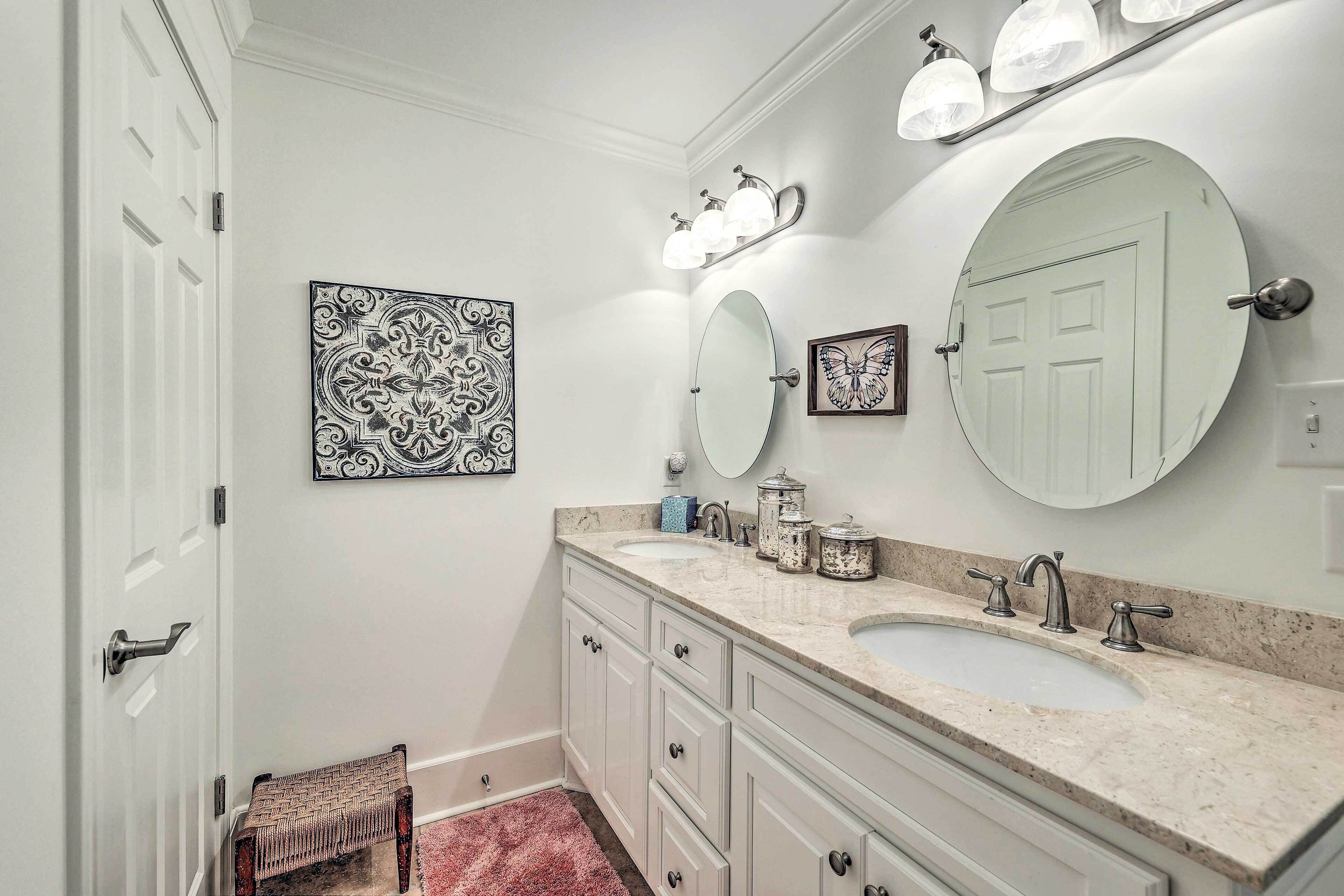A bathroom with two sinks, a large mirror, wall sconces, and decorative items.