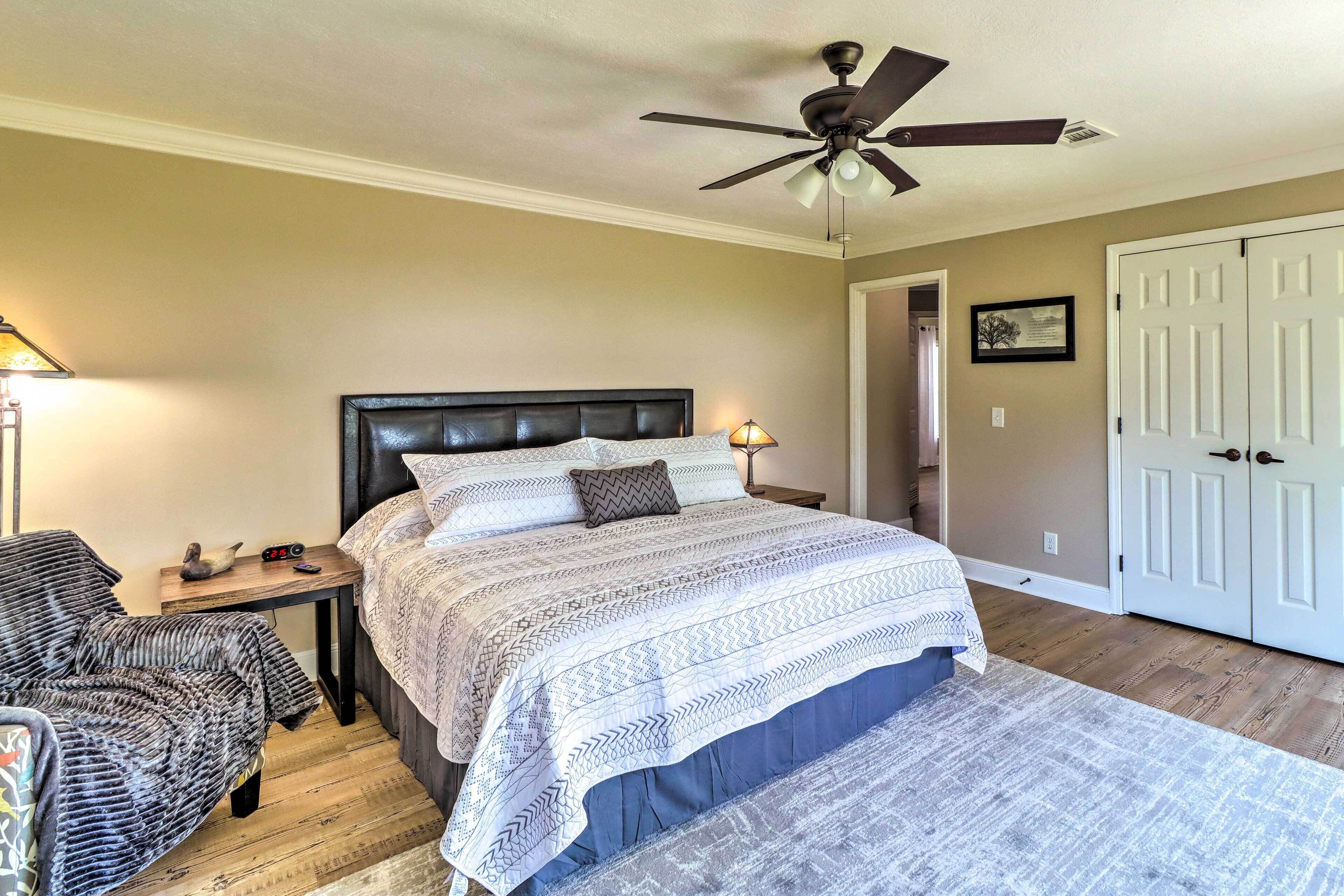 A bedroom with a bed, nightstand, chair, and a ceiling fan.