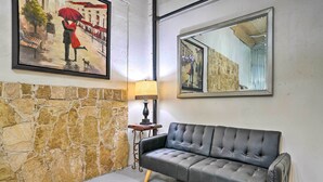 A room with a stone wall, a black leather sofa, a lamp, and two framed artworks. - Laredo Vacation Rental - Minutes From Attractions! (Laredo)
