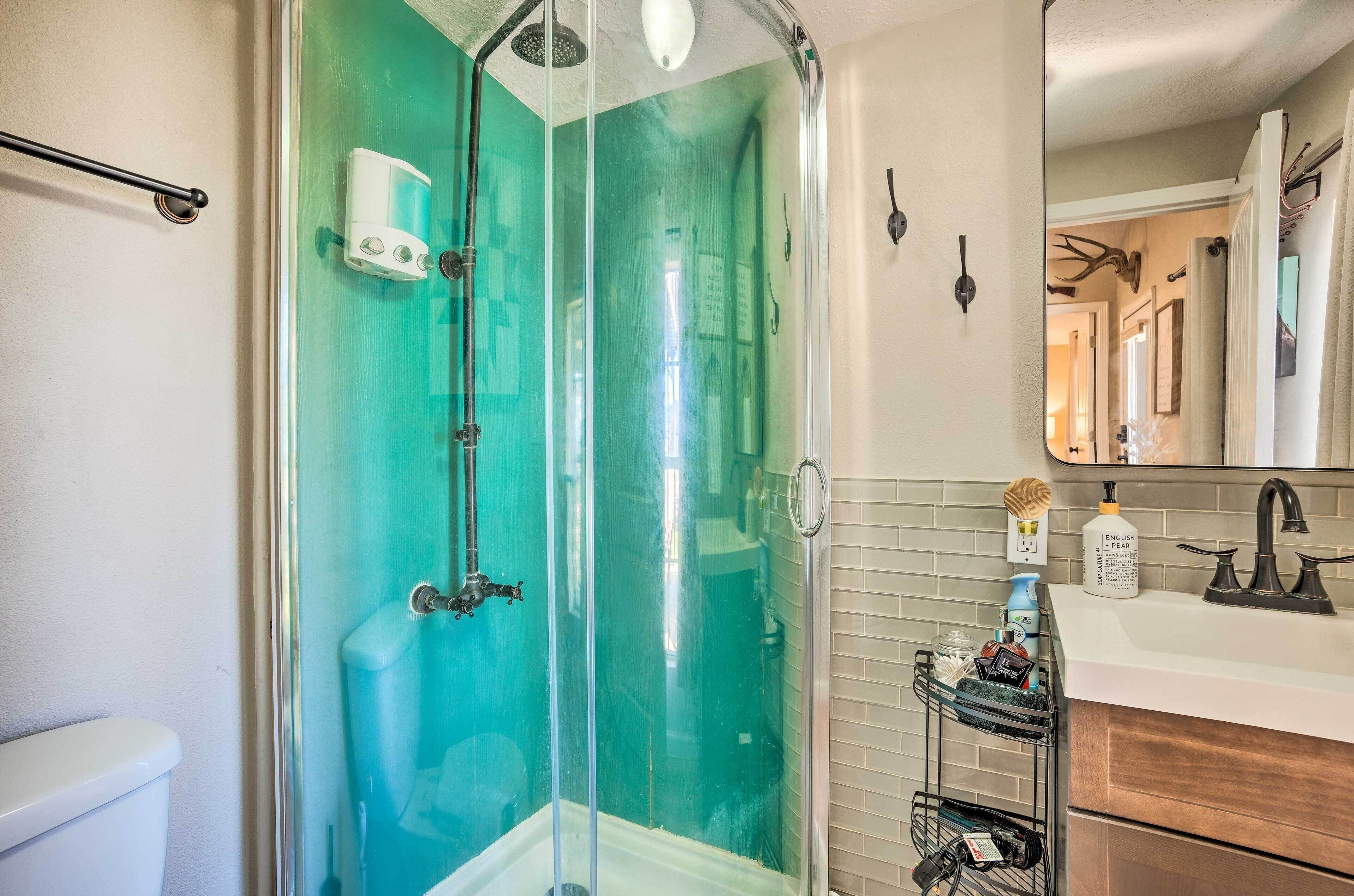 A bathroom with a glass-enclosed shower, a white toilet, a sink with a black faucet, and a mirror with a deer antler decoration.