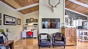A spacious living room with a wooden ceiling, a mounted deer skull, a TV, and a kitchen area with cabinets and a stove. - Private Rockaway Beach Retreat: 2 Blocks to Ocean! (Rockaway Beach)