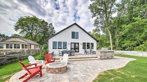 A house with a patio area featuring a stone fire pit, red Adirondack chairs, and a stone wall. - Newly Built Gilletts Lake Gem: Dock & Hot Tub (Jackson)