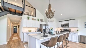 A modern kitchen with white cabinetry, a central island with bar stools, a chandelier, and a view of the living area. - Newly Built Gilletts Lake Gem: Dock & Hot Tub (Jackson)