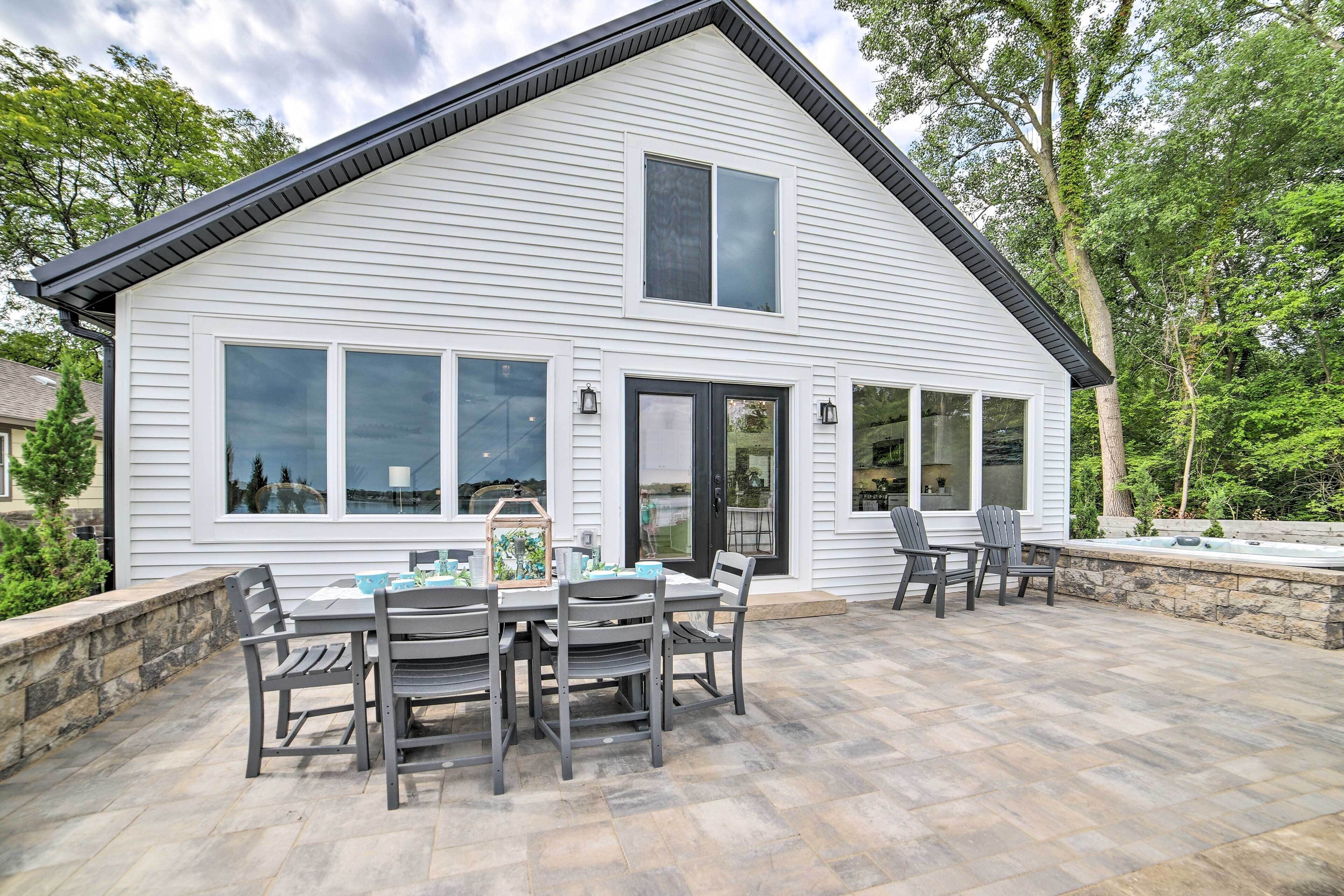 A two-story house with a patio area featuring a table and chairs, a hot tub, and a stone wall.
