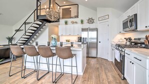 A modern kitchen with a central island, stainless steel appliances, and a staircase with a chandelier. - Newly Built Gilletts Lake Gem: Dock & Hot Tub (Jackson)