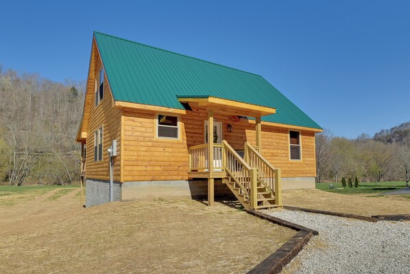 A wooden cabin with a green roof, a wooden staircase, and a gravel driveway.