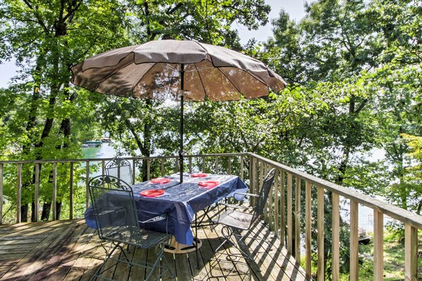 A wooden deck with a table and chairs, an umbrella, and a view of a lake. - Waupaca Lakefront Home w/ Pool Table & Dock! (Waupaca)