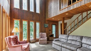 A spacious living room with a large gray sectional sofa, a pink armchair, and a wooden staircase. - Waupaca Lakefront Home w/ Pool Table & Dock! (Waupaca)