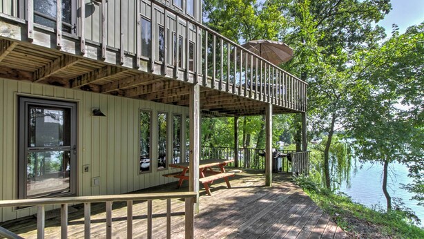A wooden deck with picnic tables and a covered area overlooking a lake. - Waupaca Lakefront Home w/ Pool Table & Dock! (Waupaca)