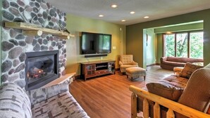 A cozy living room with a stone wall, a fireplace, a flat-screen TV, and comfortable seating. - Waupaca Lakefront Home w/ Pool Table & Dock! (Waupaca)