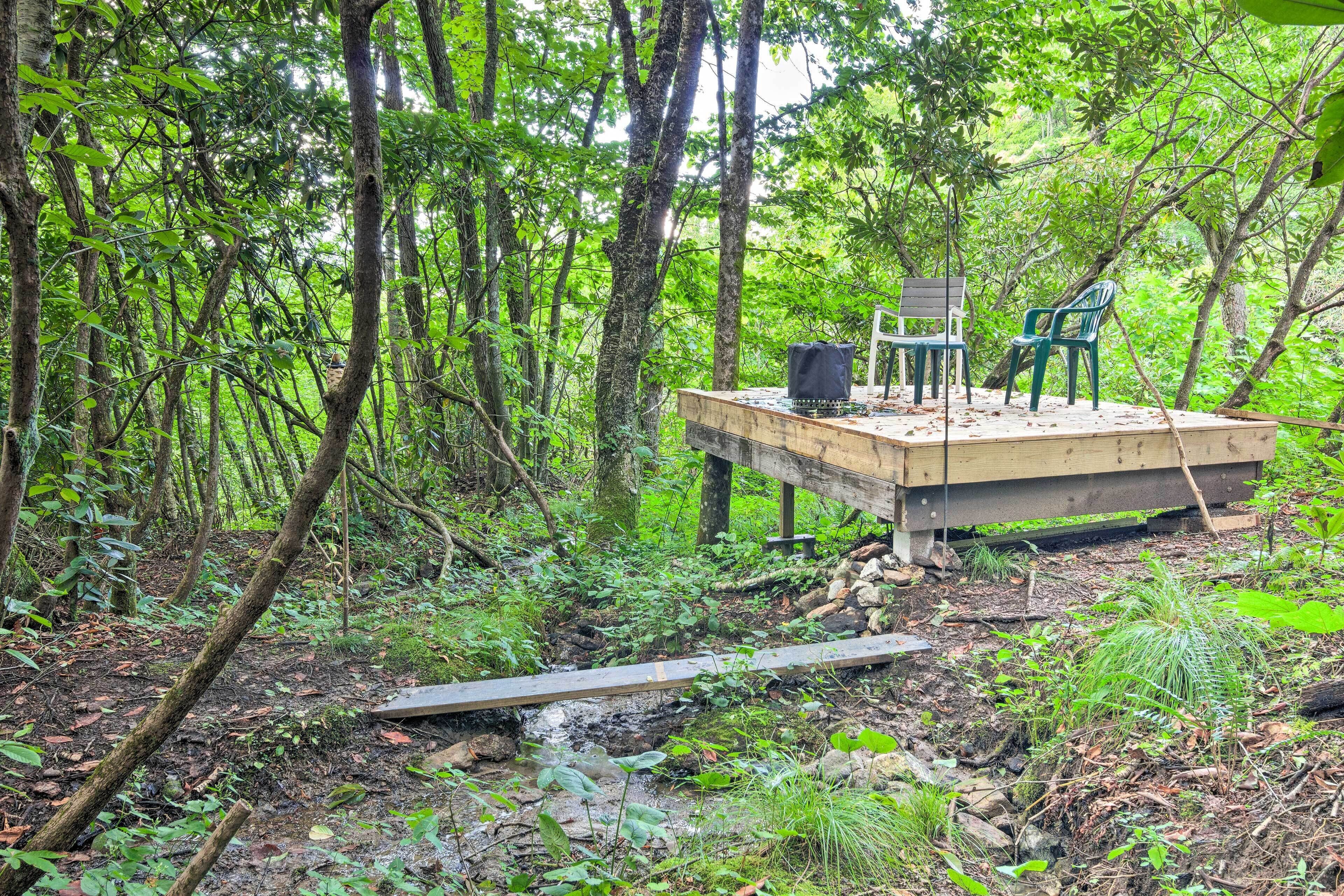 A wooden deck with two chairs and a table in a forested area.