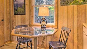 A wooden-paneled room with a glass table, two chairs, a lamp, and a framed picture on the wall.