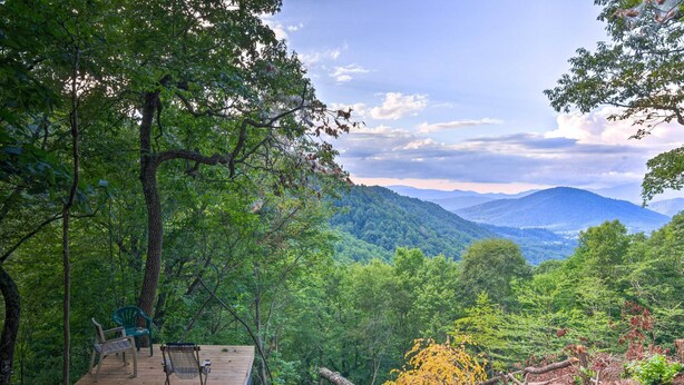 A wooden deck with two chairs and a table, overlooking a forested mountain range.