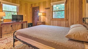 A bedroom with a bed, a desk with a television, and two windows.