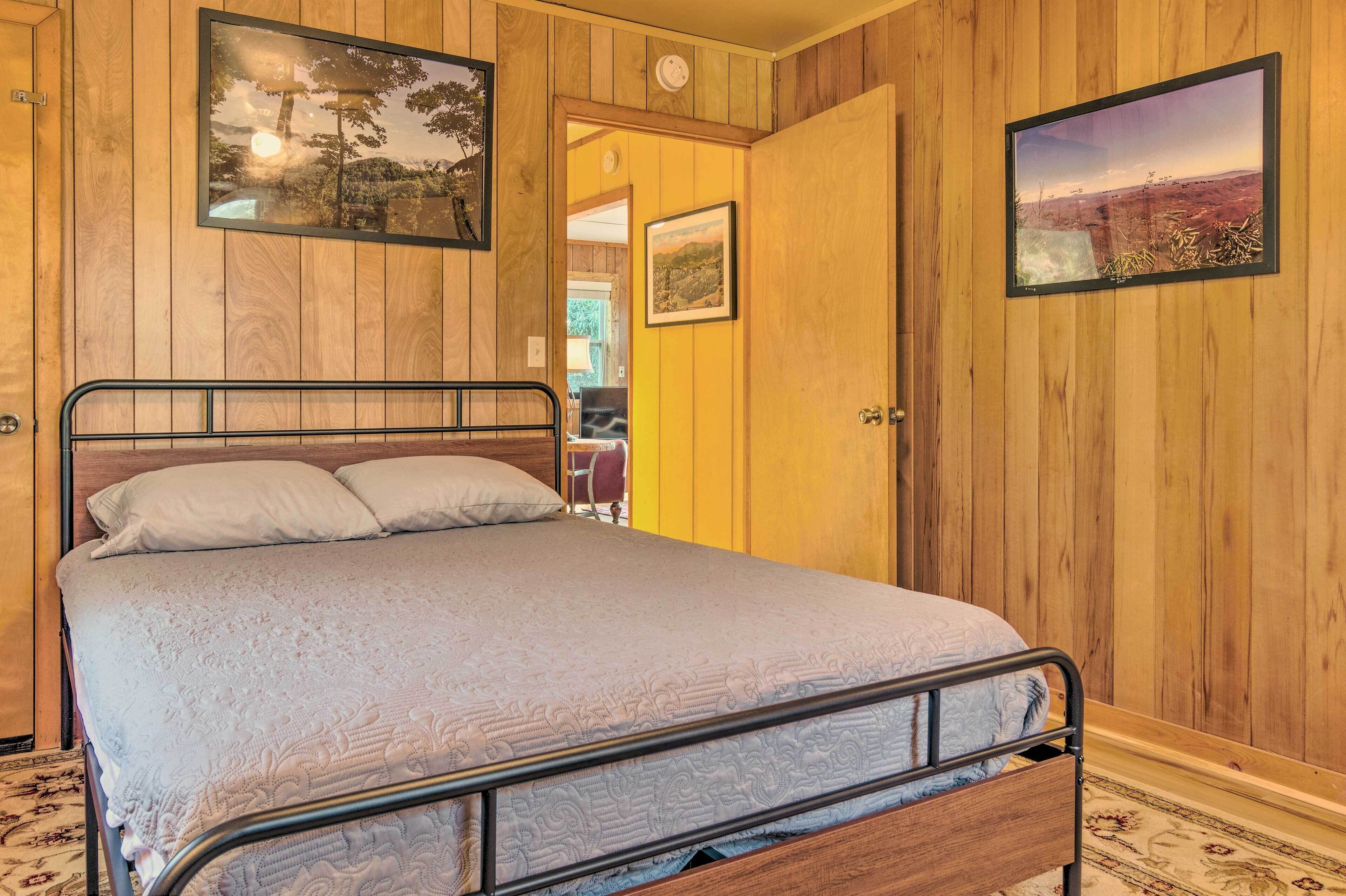 Ein Zimmer mit Holzwänden, einem Bett, zwei gerahmten Bildern und einer Tür zu einem anderen Raum.