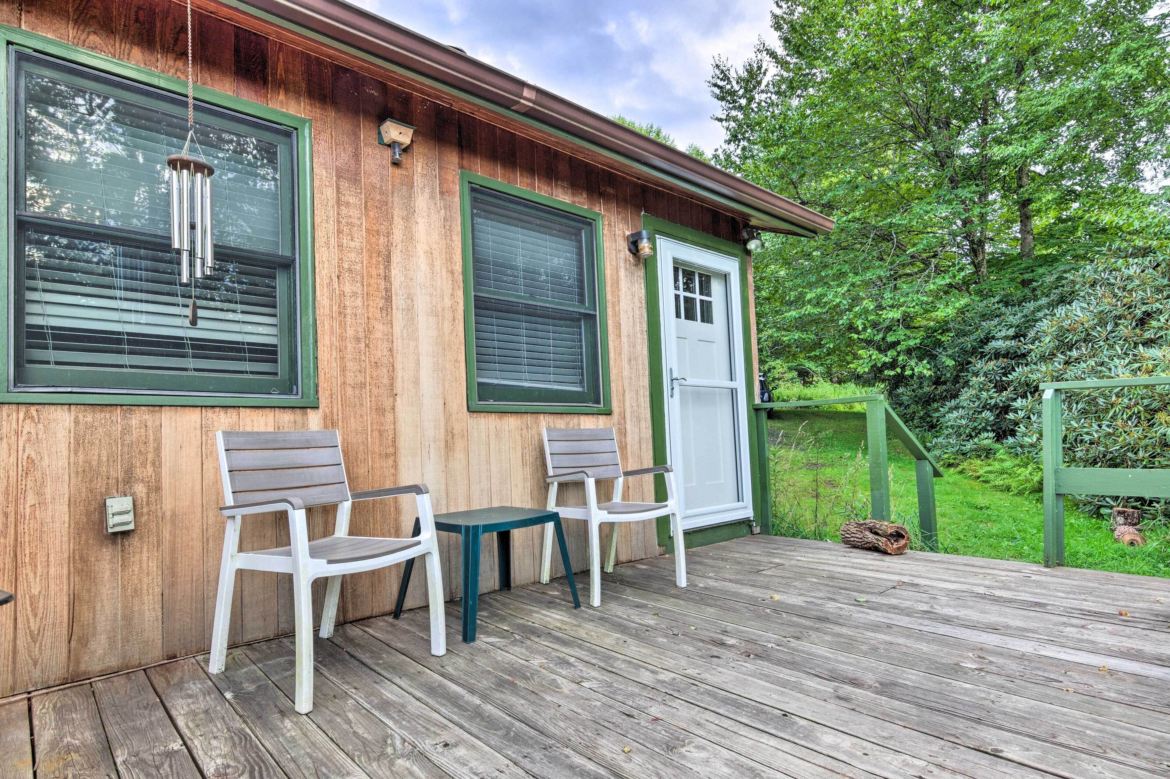 A wooden deck with two white chairs and a small table, a white door, and a green railing.
