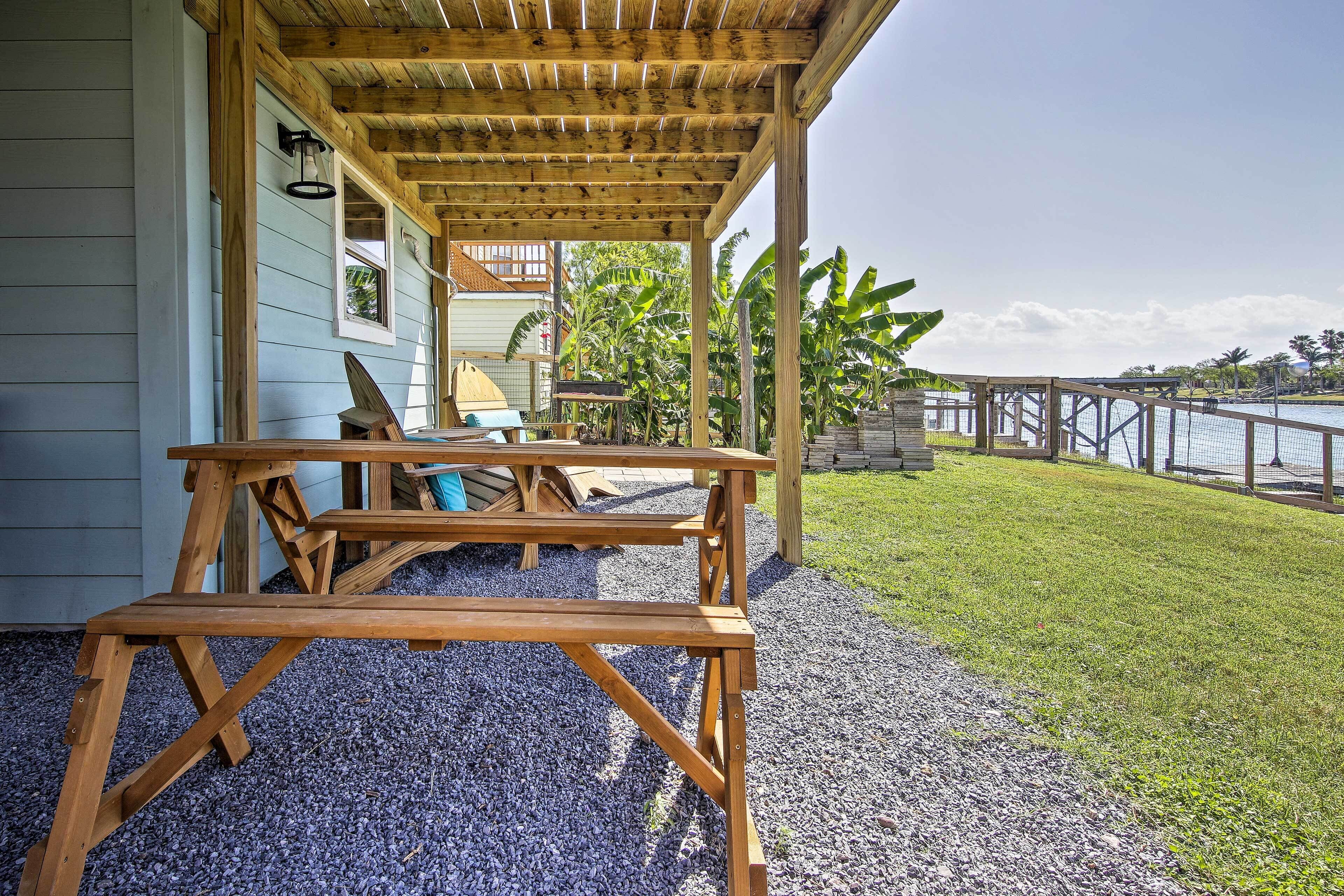 A wooden deck with a table and chairs, a covered area with a pergola, and a view of a body of water with a dock.