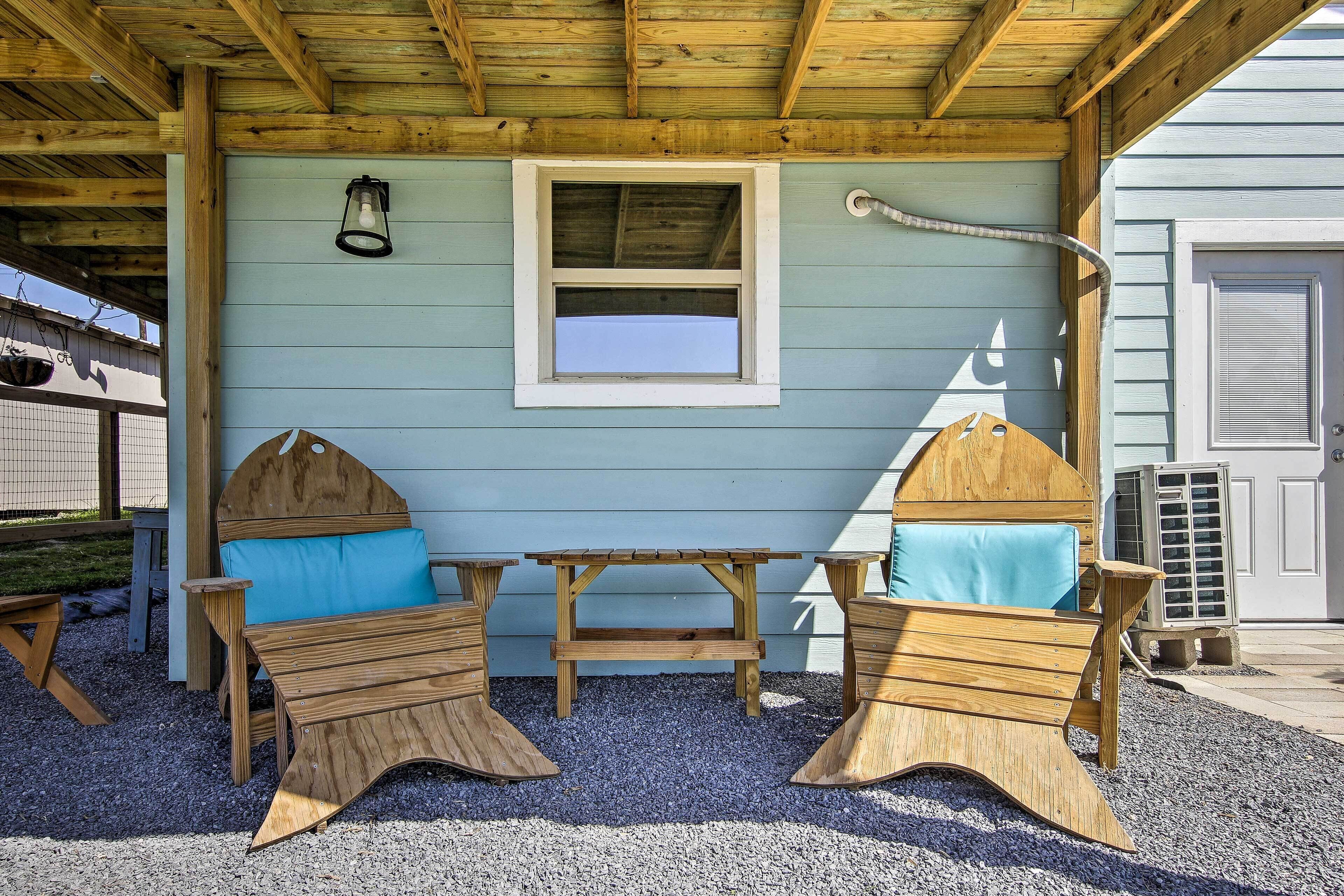 A wooden outdoor seating area with a table and two chairs, a window, and a hanging light fixture.