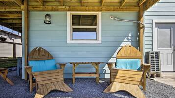 A wooden outdoor seating area with a table and two chairs, a window, and a hanging light fixture.
