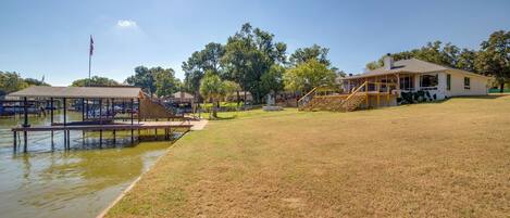 A lakeside property with a dock, grassy area, and a house with a porch.