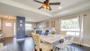 Uma sala de jantar espaçosa com uma mesa grande e cadeiras, um ventilador de teto e vista para a cozinha e a sala de estar.
