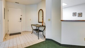 Un couloir propre et bien éclairé, avec une porte, un banc, un miroir et un petit espace d’accueil agrémenté de tableaux encadrés.