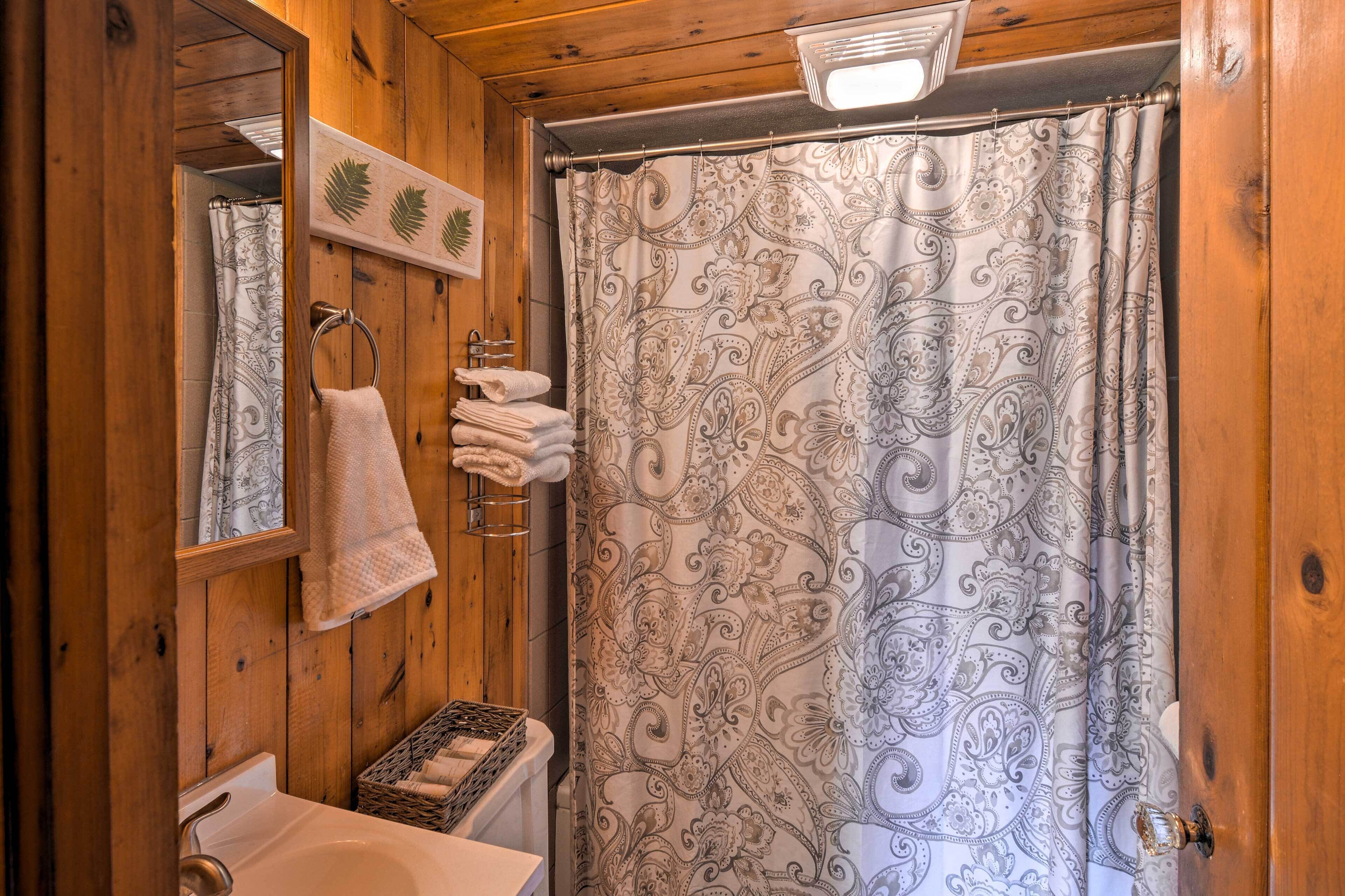 A wooden bathroom with a sink, mirror, and patterned shower curtain.
