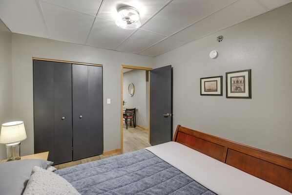 A hotel room with a bed, a desk, a chair, a lamp, and two doors.
