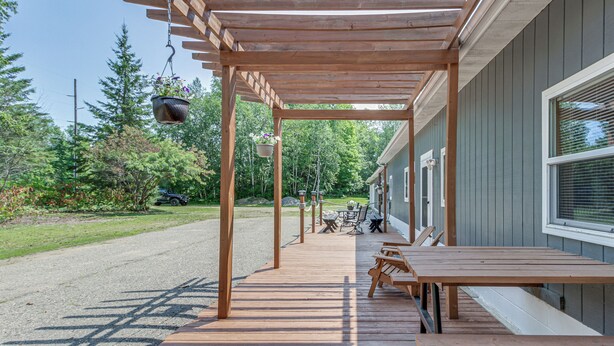 A wooden deck with benches and hanging planters, leading to a building with a covered patio area.