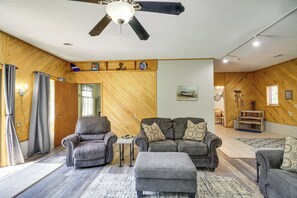 A spacious living room with a ceiling fan, leather sofas, a coffee table, and a wooden wall with a herringbone pattern.