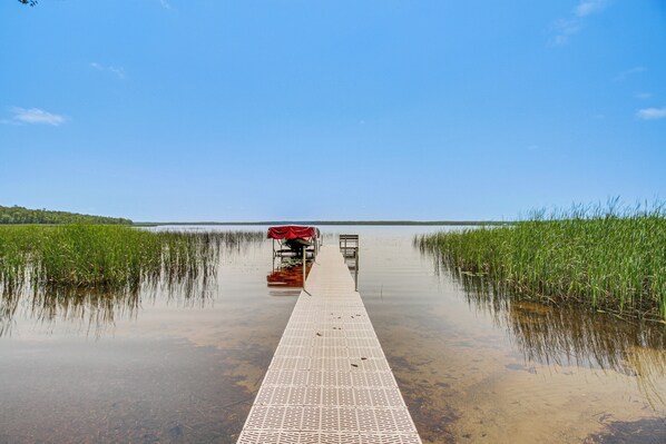 A long, narrow wooden dock extending into a calm body of water, surrounded by lush green vegetation.